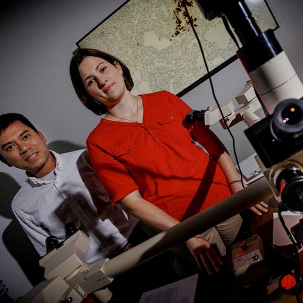Male and female scientists in front of microscope looking at camera