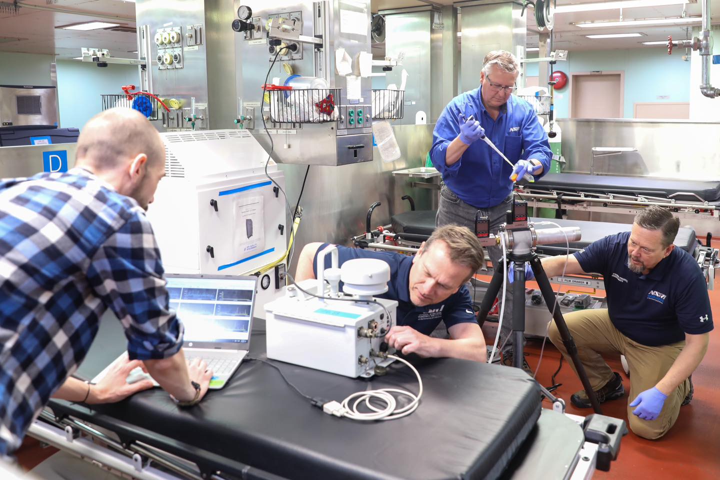 Four men setting up testing equipment for particle dispersal research onboard USNS Mercy