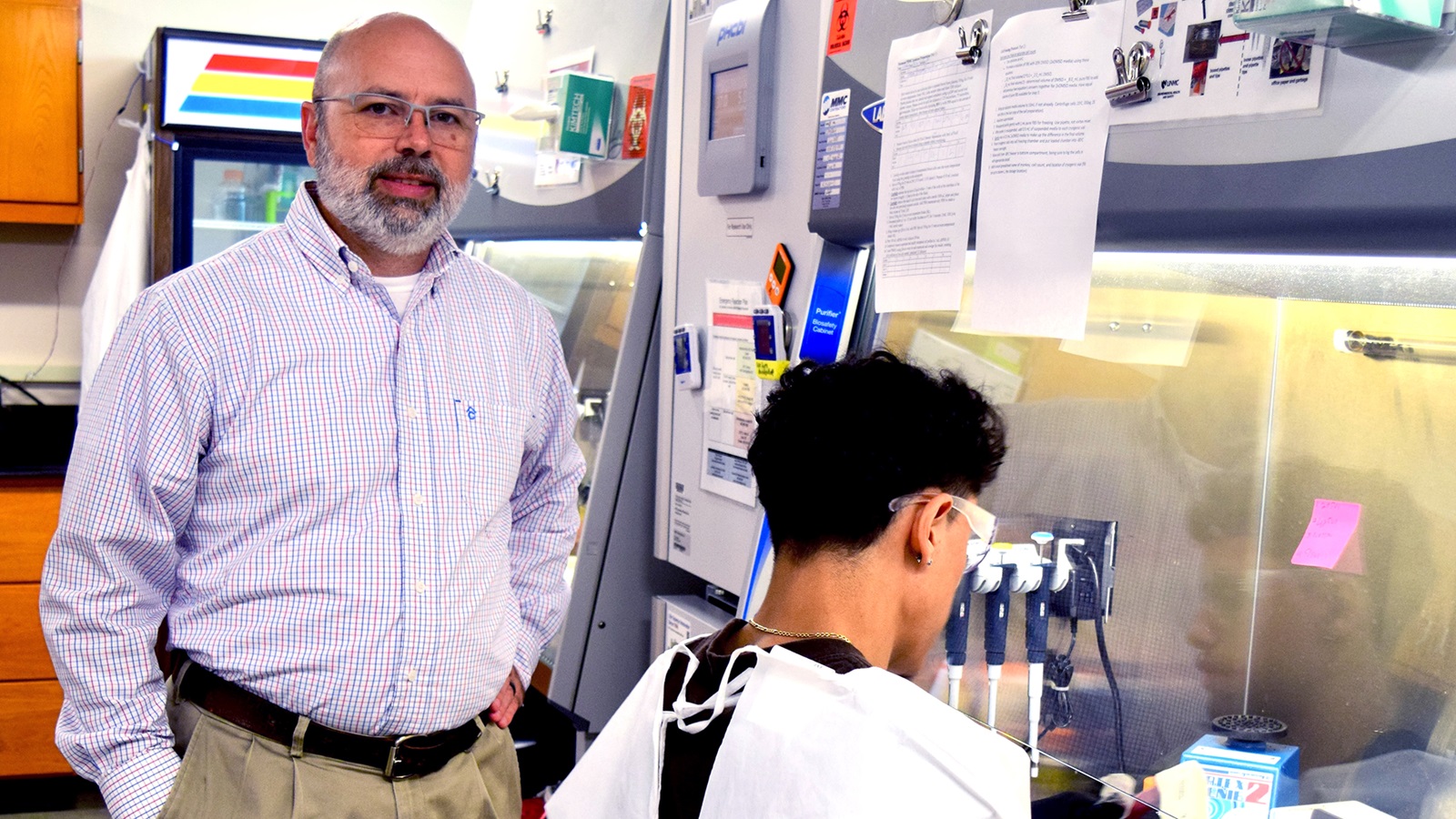 Man smiling at camera standing in laboratory. Scientist at hood.