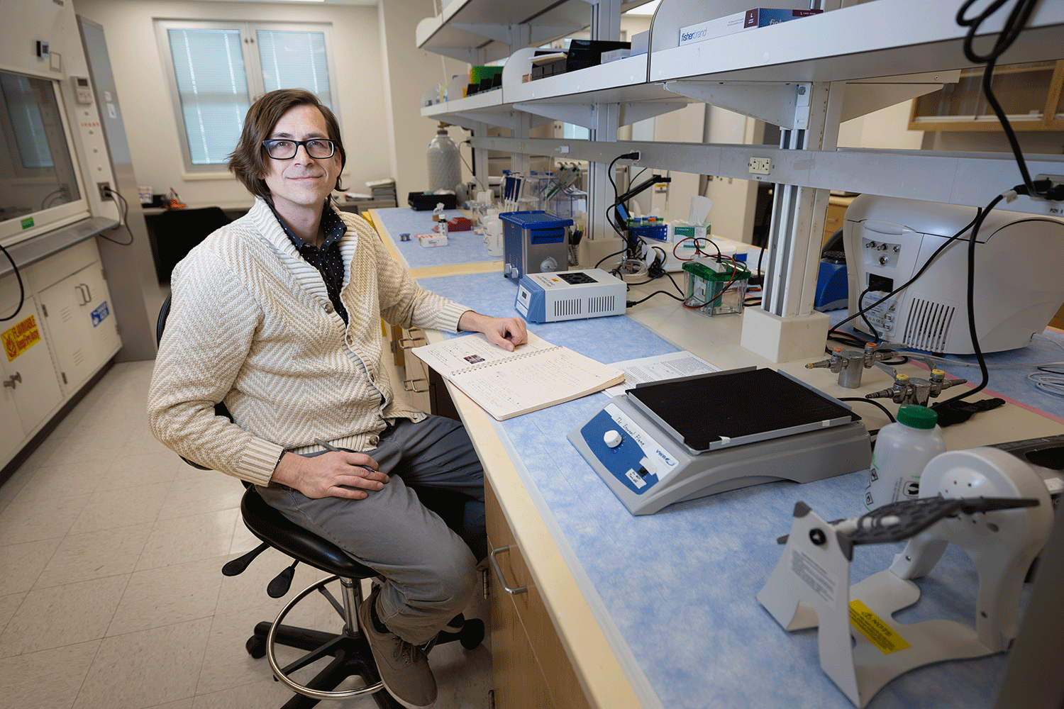 Caucasian male seated at counter in scientific laboratory surrounding by equipment