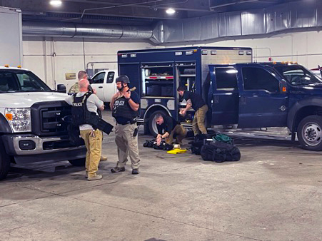 Law enforcement personnel in front of the vehicles assembling gear