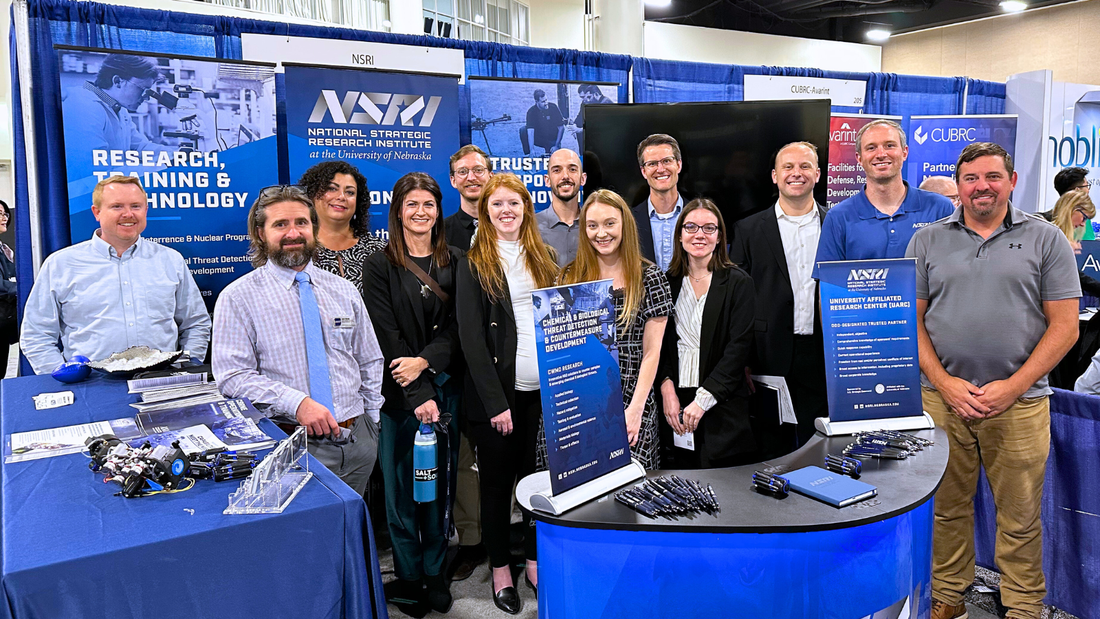 team of scientists smiling at camera at exhibit booth during conference