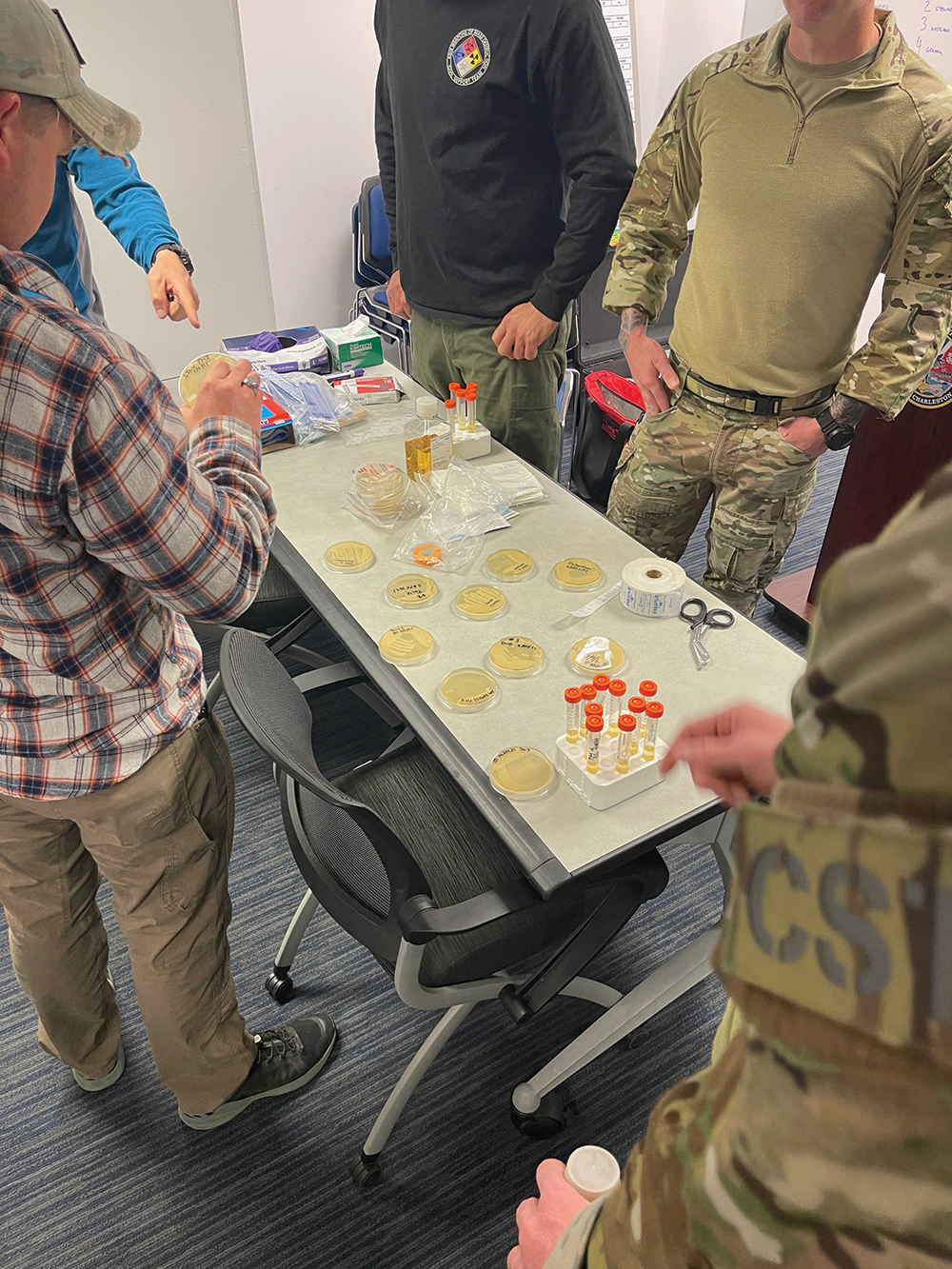 People in military uniforms standing around table of petri dishes