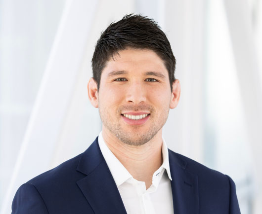 Professional headshot of a smiling Ackerman in a navy suit and white shirt against a clean, modern office background