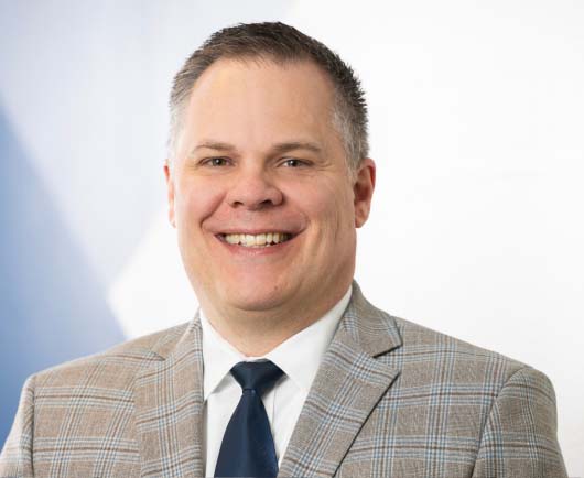 Professional headshot of David Blanchard wearing a light plaid blazer and navy tie, posed against a clean, modern background