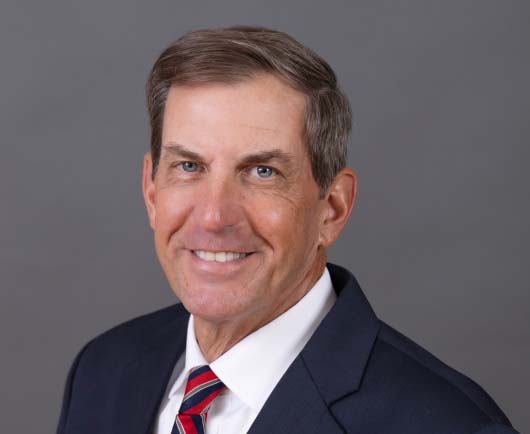 Professional headshot of David Kriete in a navy suit and striped tie, posed against a neutral gray background