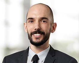 Professional headshot of Don Huston with a short beard, wearing a dark suit and tie in a bright office setting