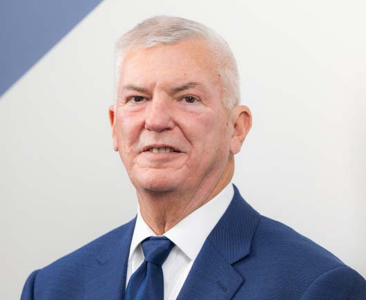 Professional headshot of Gary Gates with white hair, wearing a blue suit and tie against a clean, modern background