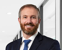 Professional headshot of Van Buren with a beard, wearing a navy suit and blue tie in a bright modern office setting