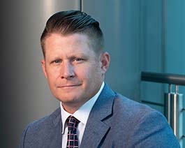 Professional headshot of Wes Carter with slicked-back hair, wearing a gray suit and patterned tie in a modern office setting