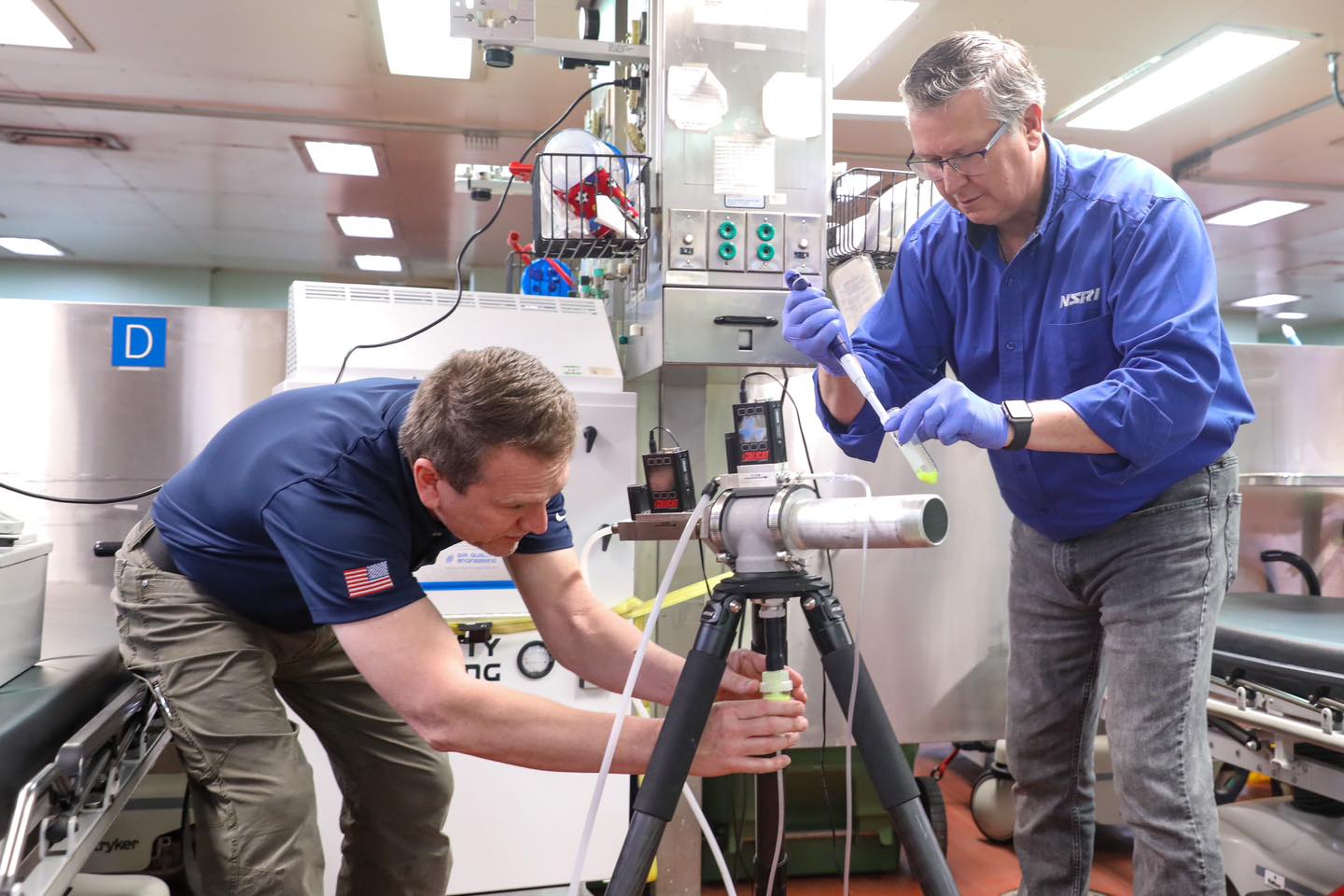 Male scientists attach a nebulizer cup to the custom aerosol generator to prepare for a tracer release .
