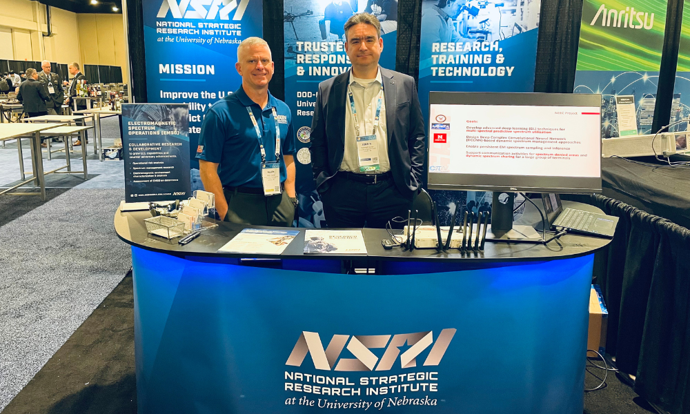 two men standing behind exhibit booth in large conference center
